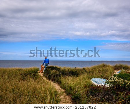 Man and his golden retriever pause in the sand dunes before walking on the beach/Man and Dog at the Beach