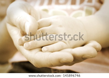 An affectionate shot of mothers hand holding her baby girls hand.  A vintage technique was used on a shollow DOF with grain added for the visual effect.