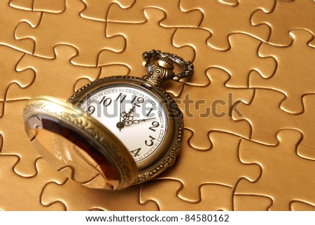 A pocket watch rests on a golden puzzle.
