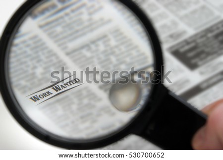 Searching for a job through the newspaper sections with a magnified glass.