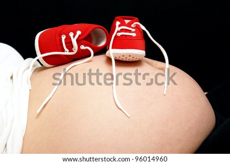 A mother lays back and rests her unborn childs shoes on her belly.