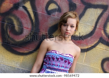 A young attractive woman poses next to some city graffiti.