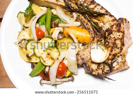 Grilled pork chop steak with roasted veggies white plate on wooden table
