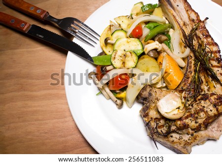 Grilled pork chop steak with roasted veggies white plate on wooden table