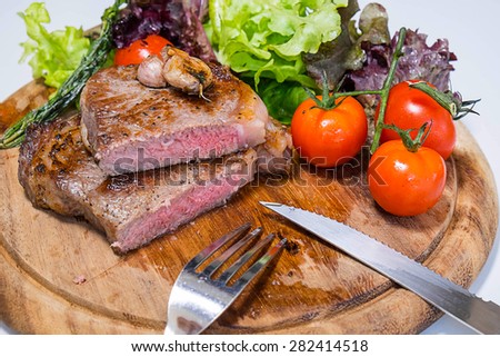 Beef rib eye steak with knife and fork for meat on cutting board