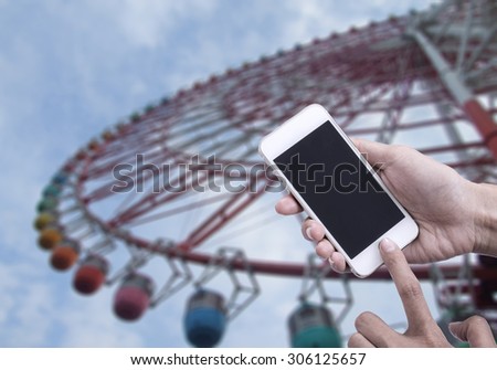 Woman holding smart phone or mobile phone with blank mobile.over Ferris wheel background for working online on vacation.