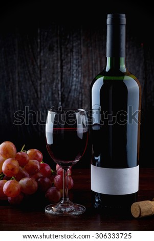 Wine Glass with bottle of red wine and cluster of grape on wooden table