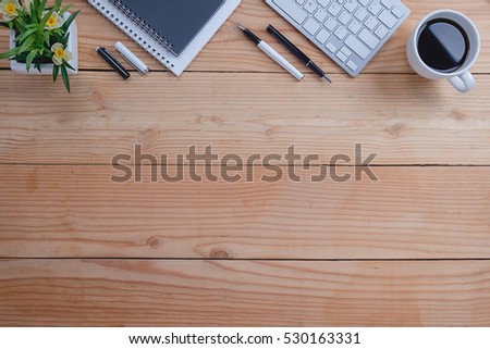 Office desk table with keyboard, notebook, pen, cup of coffee and flower. Top view with copy space (selective focus)