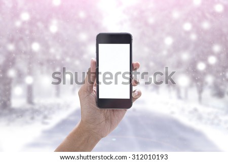 Hand holding smartphone device on snow winter background.