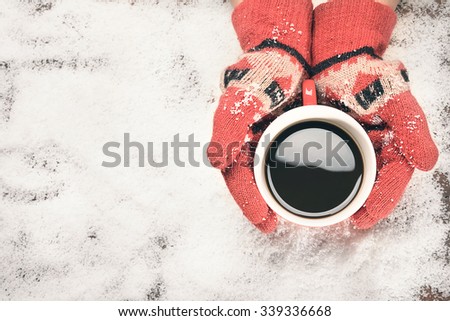 Woman hands in red teal gloves holding a coffee mug on snow vintage tone.