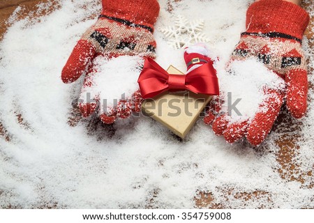 Hands in glove holding gift box on snow.