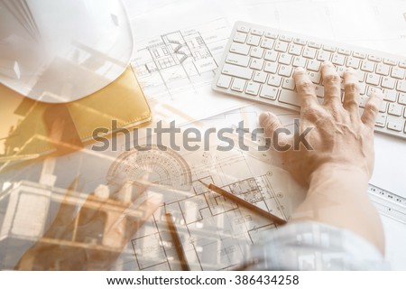 Close up of Architect working on blueprint with computer at workplace.Double exposure of construction site.