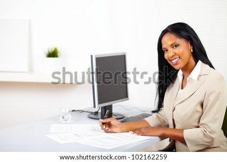 Portrait of a young professional woman on work desk, smiling and looking to you whole working on documents