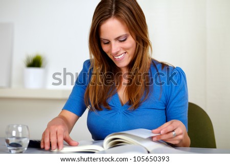 Portrait of a blonde friendly young woman reading a book on blue shirt at home indoor