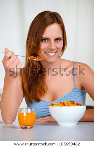 Closeup portrait of a relaxed pretty young woman eating cereals and strawberry for breakfast at home