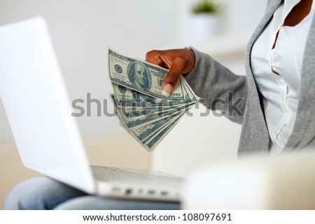 Portrait of an afro-american woman holding plenty of cash money in front a laptop