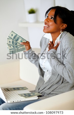 Portrait of a happy woman holding plenty of cash money while is looking up with hope