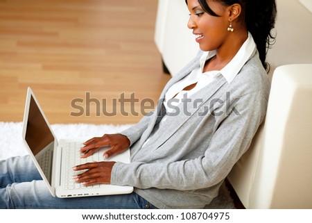 Portrait of an afro-American young woman using her laptop while sits on the floor at home indoor