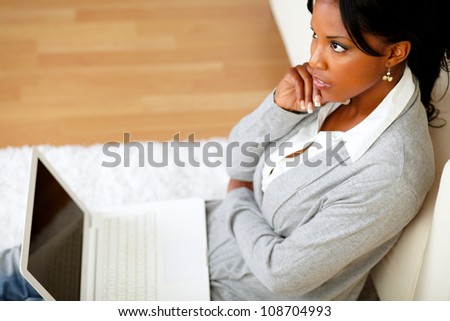 Top view portrait of a pensive young woman is sitting on the floor in front of her laptop at home indoor