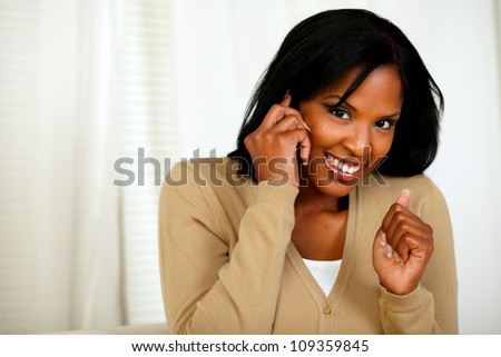 Portrait of an excited woman looking to you and conversing on mobile phone at home indoor