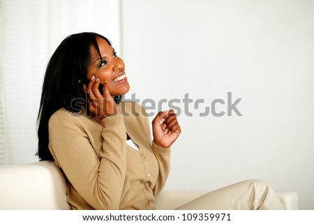 Portrait of an excited afro-American woman conversing on mobile phone while sitting on couch at home indoor