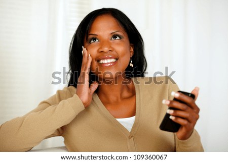 Portrait of a charming black woman holding a mobile phone while is looking up
