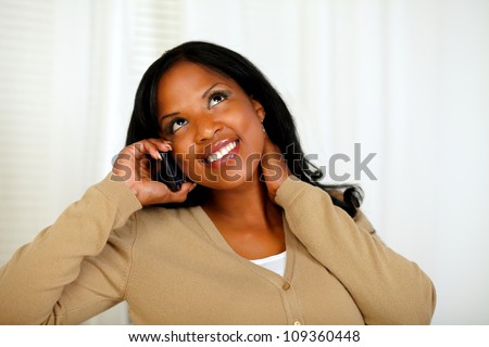 Portrait of a charming young woman conversing on mobile phone while is looking up at home