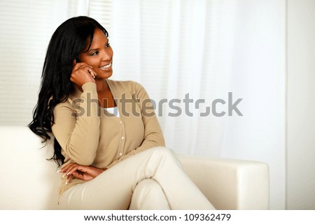 Portrait of a young woman sitting on a sofa and talking on cellphone at home indoor