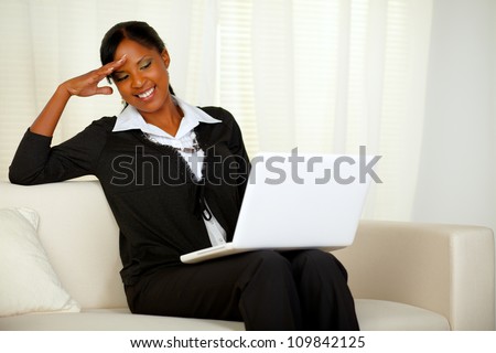 Portrait of a charming executive black woman reading on laptop screen. Sitting on a couch and laughing and having fun while working at home