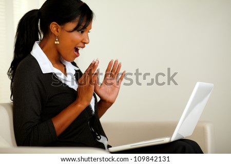 Portrait of a surprised executive young woman reading a great business news on laptop while sitting on couch