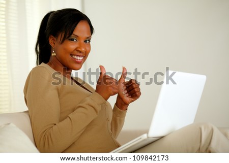 Portrait of a positive afro-American woman in front her laptop while looking at you and lifting the fingers up