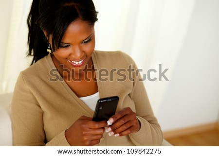 Top view portrait of a young afro-american female sending a message while sitting on sofa at home indoor