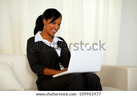 Portrait of an attractive woman on black suit working on laptop while sitting on couch at home indoor