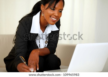 Portrait of a charming businesswoman on black suit working while sitting on couch in front of her laptop