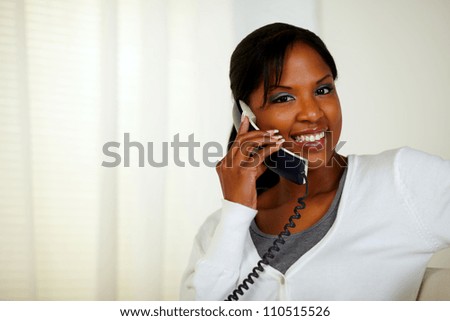 Portrait of a smiling black woman looking at you while talking on phone at soft colors composition
