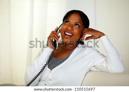 Portrait of a relaxed pretty young woman conversing on phone while sitting on sofa and looking up at home indoor