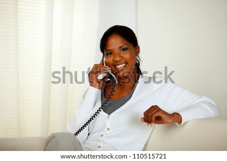 Portrait of an afro-American woman smiling at you while conversing on phone at home indoor