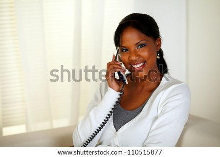 Portrait of a relaxed woman looking at you while talking on phone at home indoor