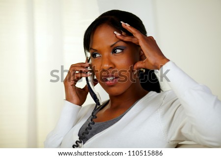 Portrait of a young woman conversing on phone with headache at home indoor