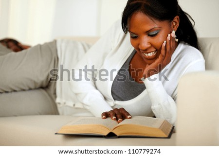 Portrait of a stylish young relaxed woman reading a book while lying on sofa at home indoor