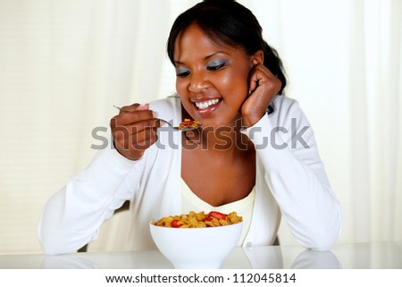 Portrait of an afro-american young woman eating a bowl of cereals with strawberries at soft colors composition