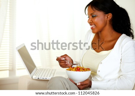 Portrait of a relaxed young woman having healthy breakfast and using her laptop at home indoor
