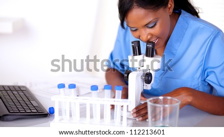 Scientific woman in blue uniform working at laboratory with a microscope