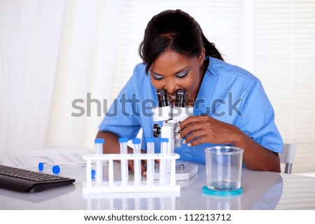 Afro-american scientific woman in blue uniform working at laboratory with a microscope and test tube