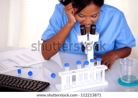Afro-american scientific girl in blue uniform working at laboratory with a microscope and test tube