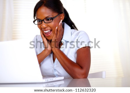 Excited woman looking to laptop screen with black glasses at workplace - copyspace
