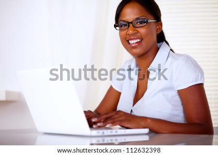 Pretty woman looking at you with black glasses while working on laptop