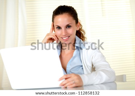 Smiling young female looking at you in front of her laptop at home