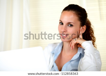 Stylish young woman looking at you while using her laptop