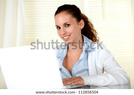 Smiling young woman looking at you in front of her laptop